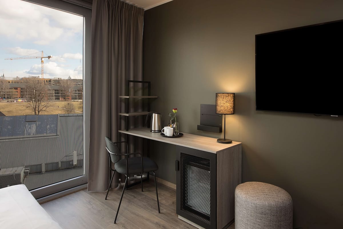 Habitació d'hotel moderna amb un gran finestral, una escriptori amb cadira, una televisió i un petit otomà.