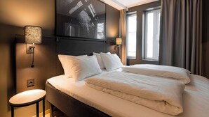 A hotel room with a large bed, two bedside lamps, a wall-mounted TV, and a window with curtains. - Scandic Vulkan (Oslo)