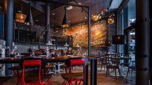 A modern restaurant with exposed brick walls, wooden flooring, and red bar stools. - Scandic Vulkan (Oslo)