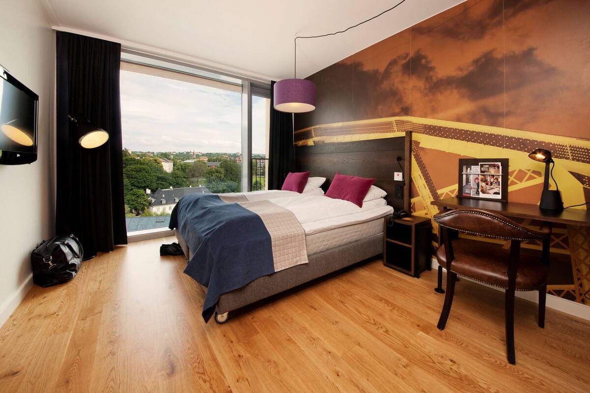 Una habitació d'hotel moderna amb un llit gran, un escriptori i vista a la ciutat.