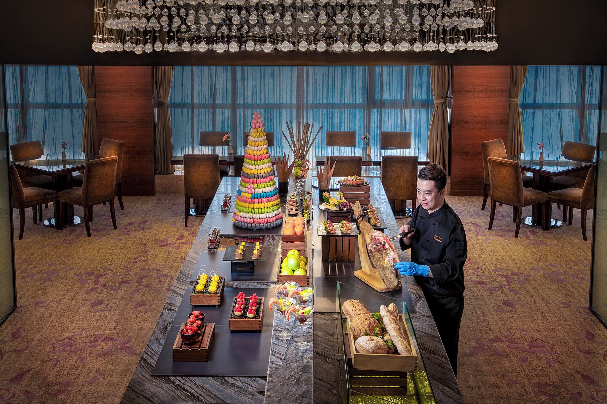 A hotel dining area with a long table set for a meal, a decorative centerpiece, and a person serving food.