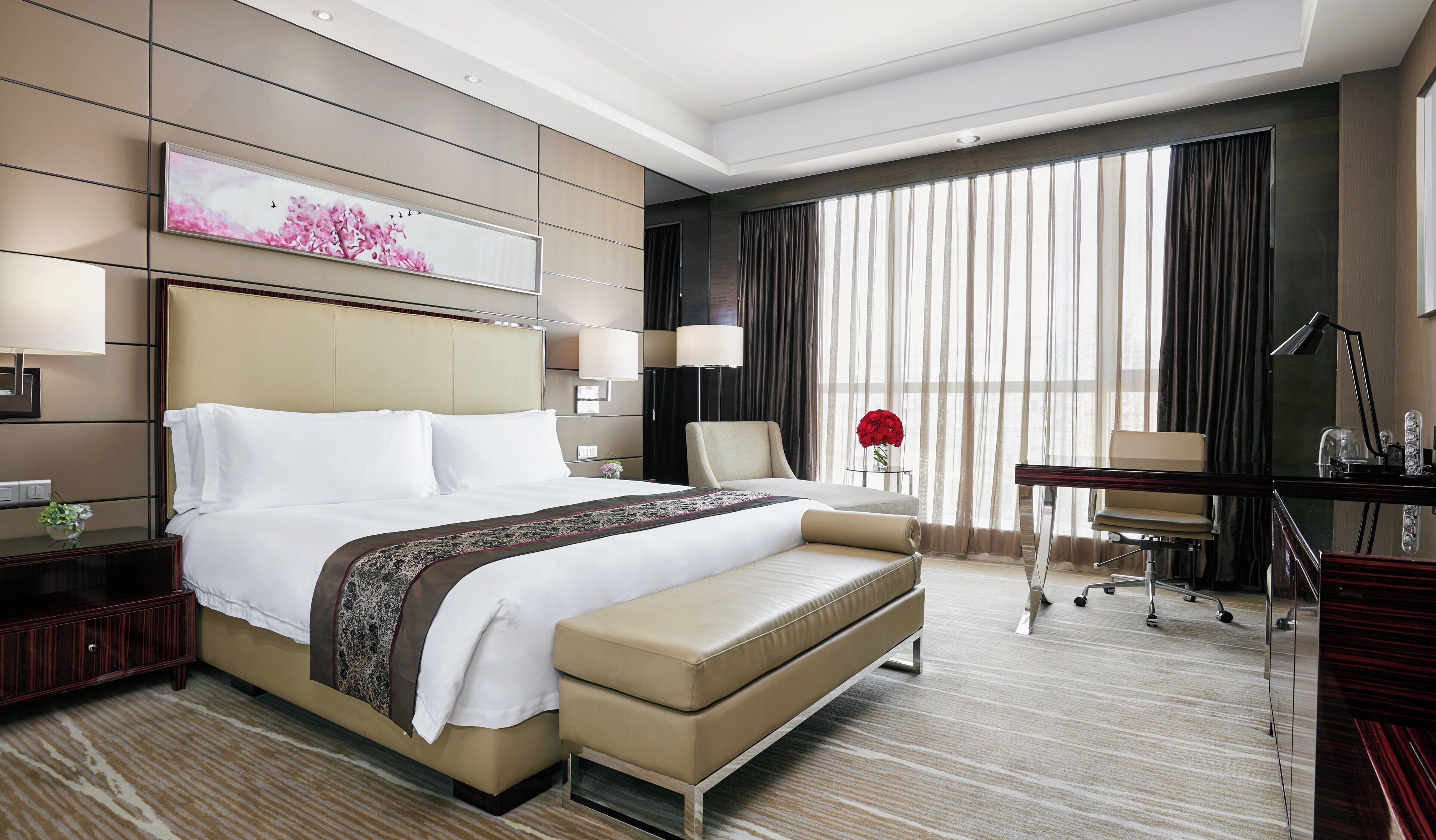 A hotel room with a large bed, a desk, a chair, and a large window with curtains.