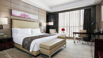 A hotel room with a large bed, a desk, a chair, and a large window with curtains.