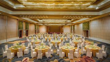A large banquet hall with round tables set for a formal event, featuring a patterned carpet and a chandelier.
