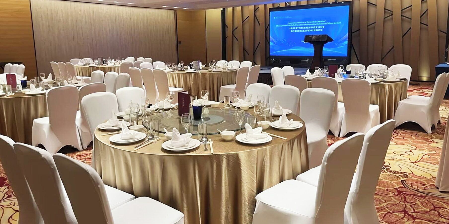 A conference room with round tables set for a meeting, white chairs, and a large screen displaying a presentation.
