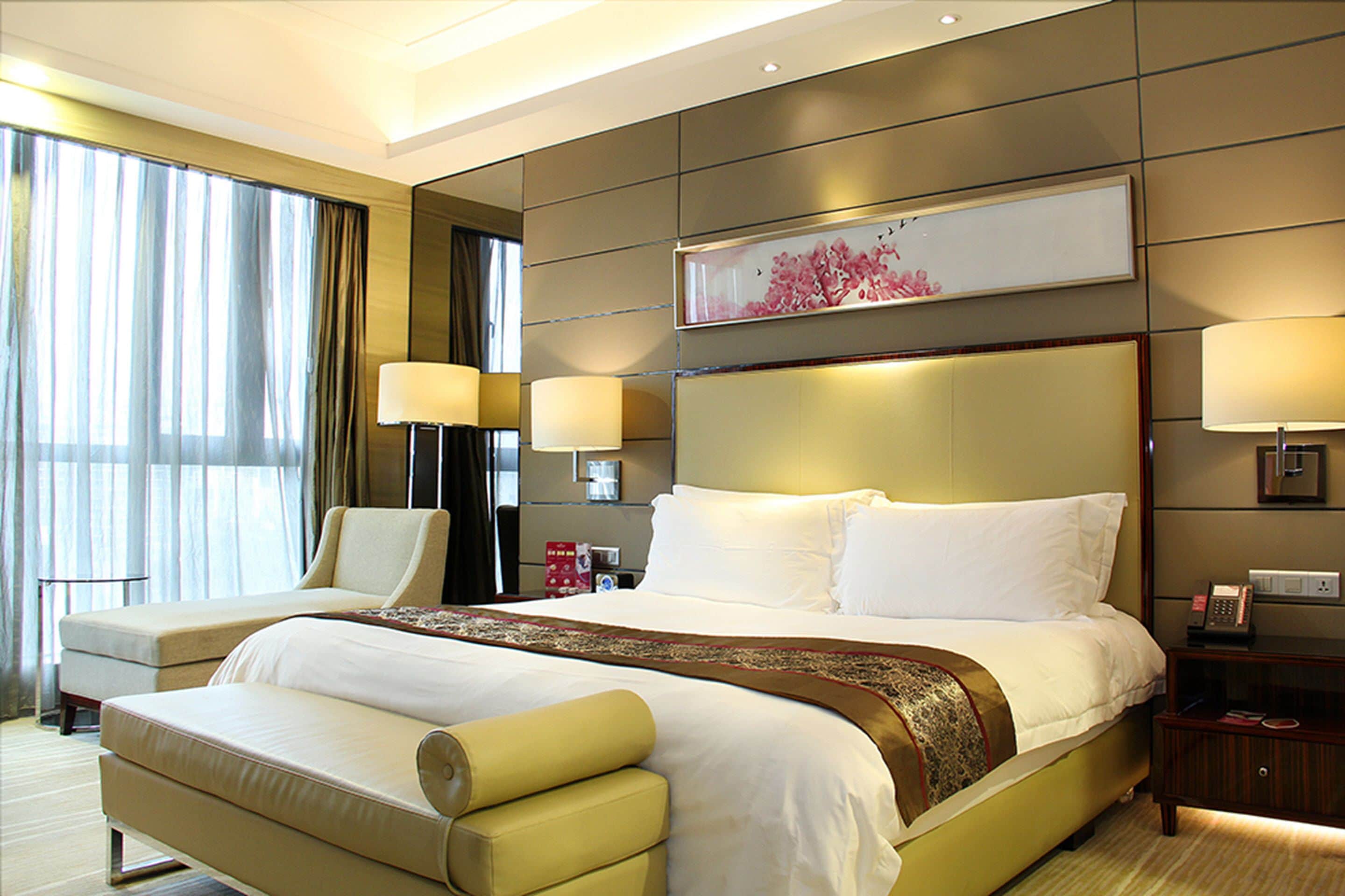 A hotel room with a large bed, a sitting area, and a view of the city.