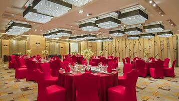 A banquet hall with round tables, red chairs, and chandeliers.