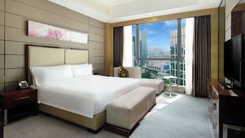 A modern hotel room with a large bed, a TV, a desk, and a view of the cityscape.