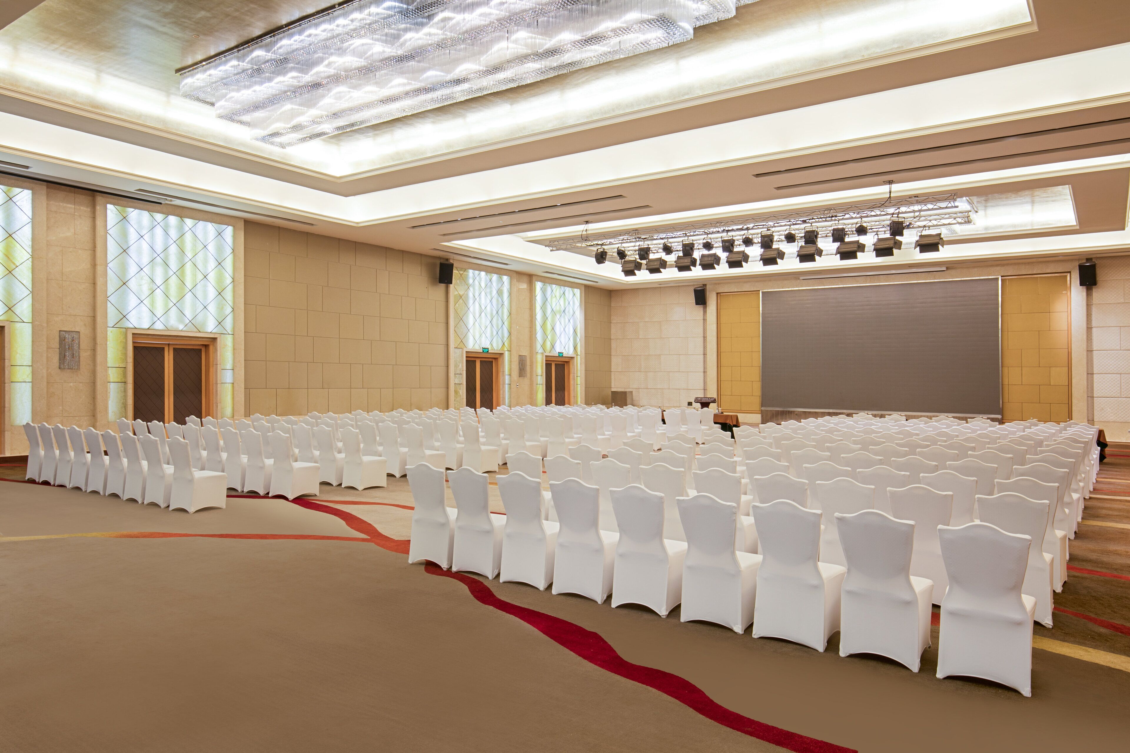 Una sala conferenze con file di sedie bianche, un grande schermo e un palco illuminato.