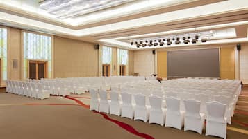 Une salle de conférence avec des rangées de chaises blanches, un grand écran et une scène éclairée.