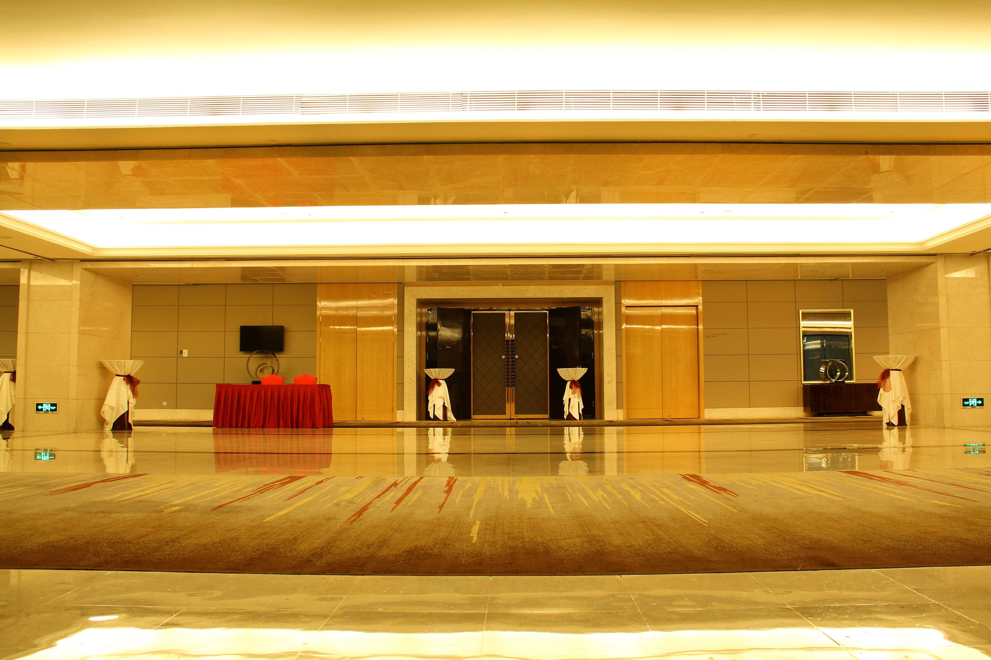 A spacious lobby with a polished floor, a red table, and a double door entrance.
