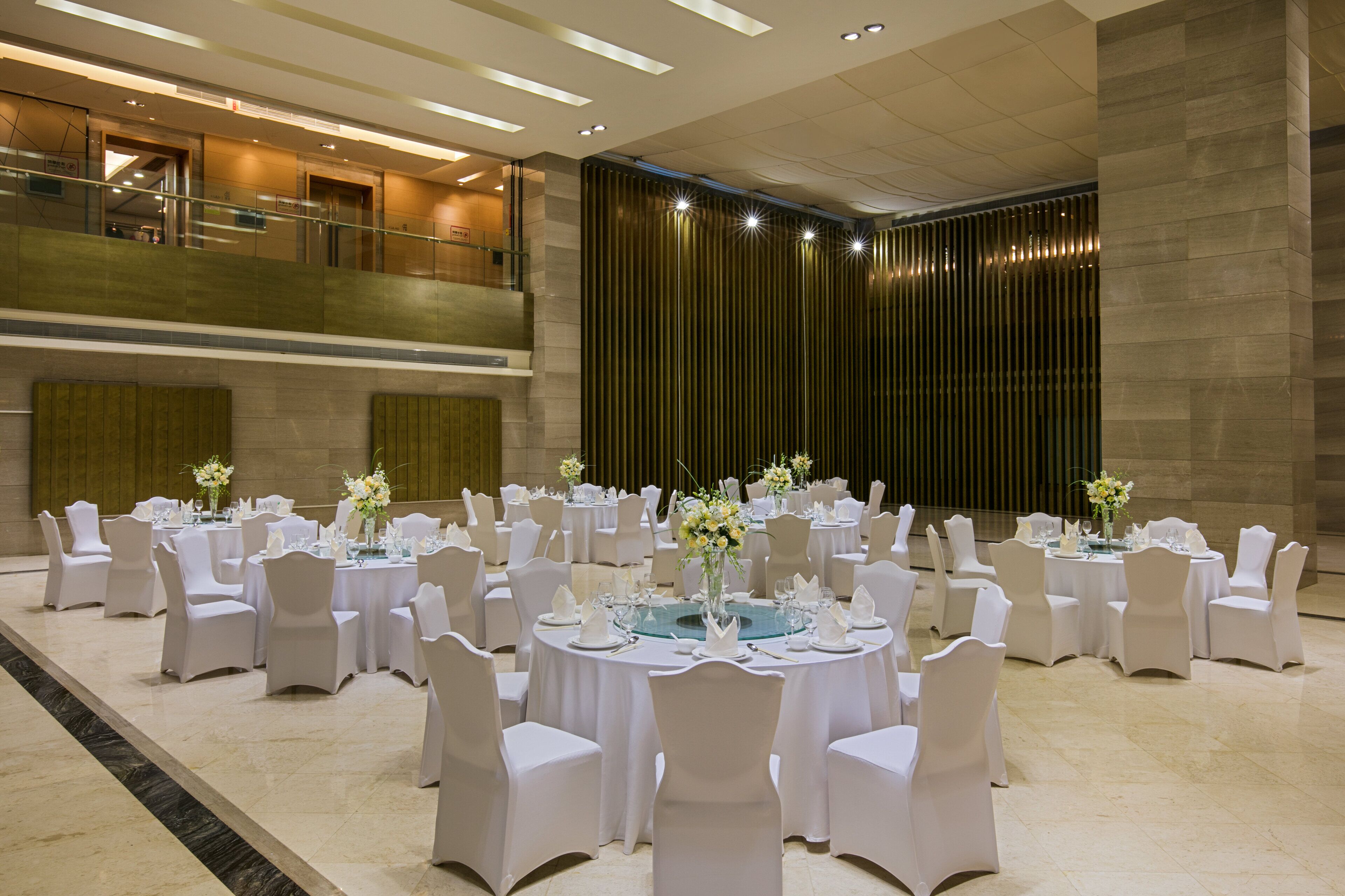 Een ruime, overdekte balzaal met meerdere ronde tafels gedekt voor een diner, elk met witte stoelen en middelpuntdecoraties.