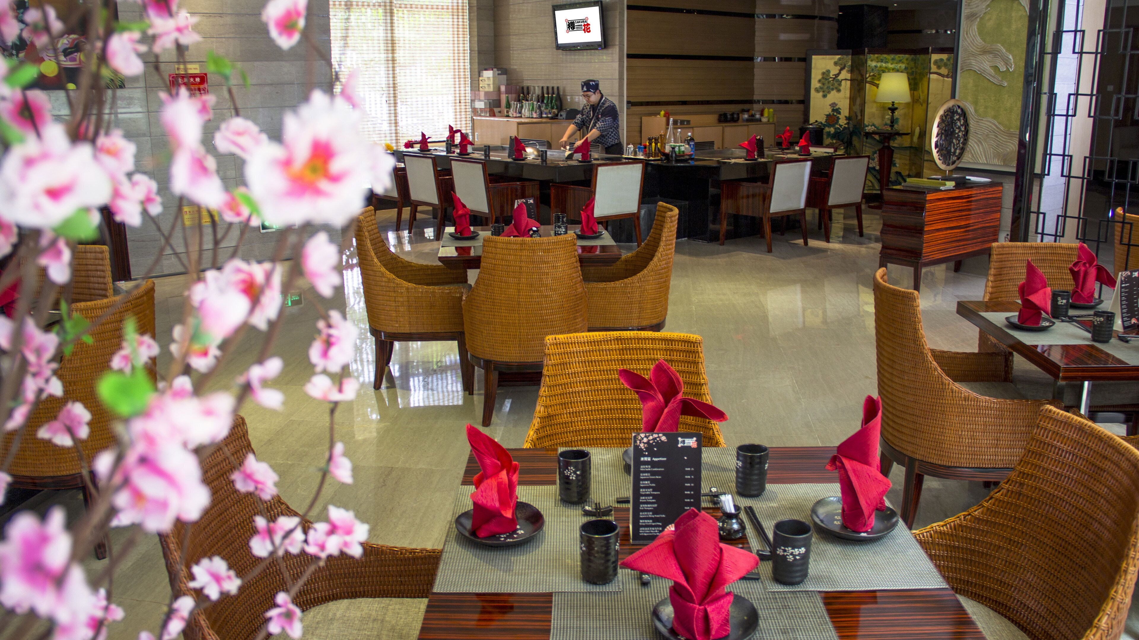 A restaurant with wicker chairs, red napkins, and a sushi bar.
