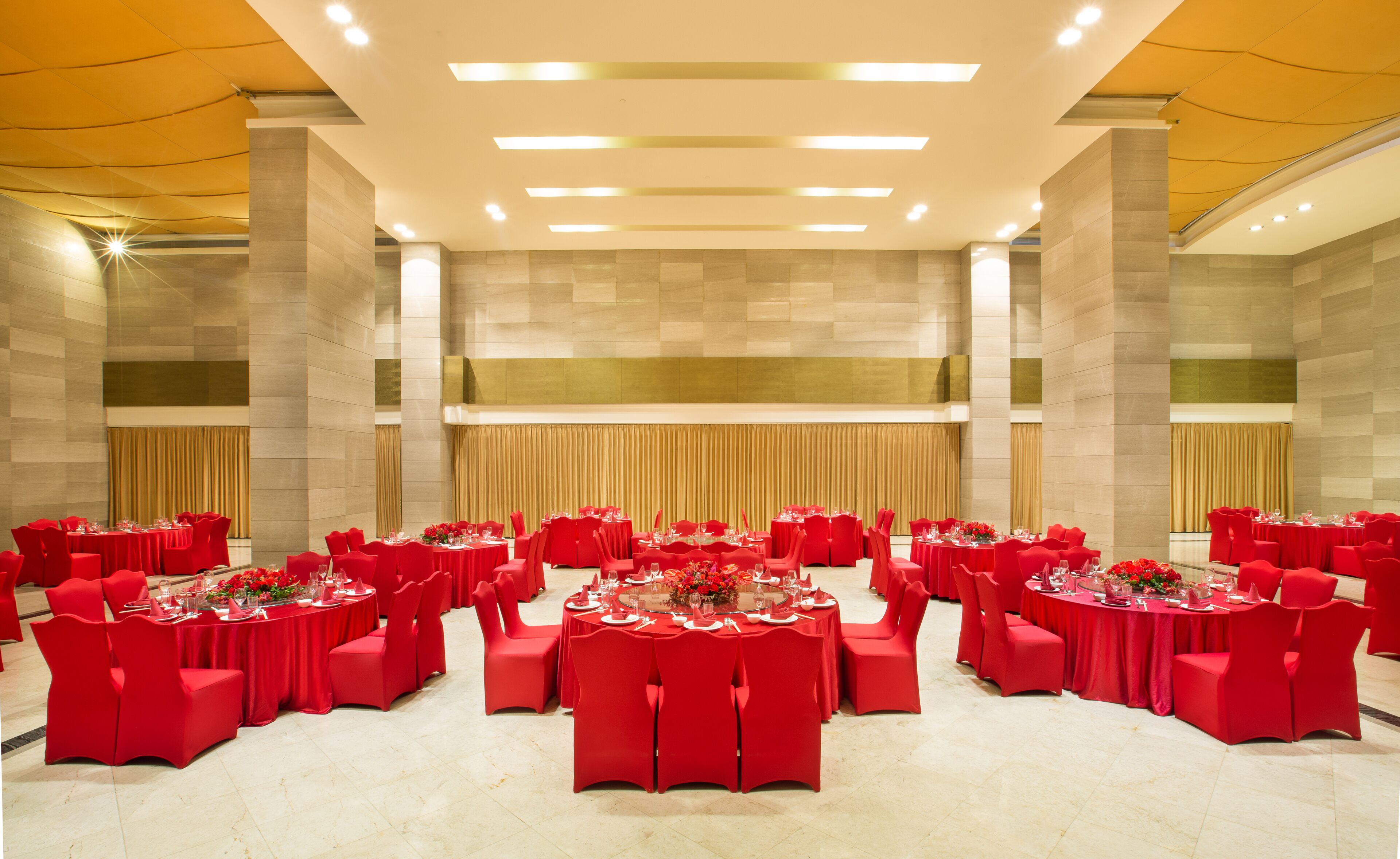 Een ruime feestzaal met meerdere ronde tafels, elk voorzien van rode stoelen en tafelkleden.