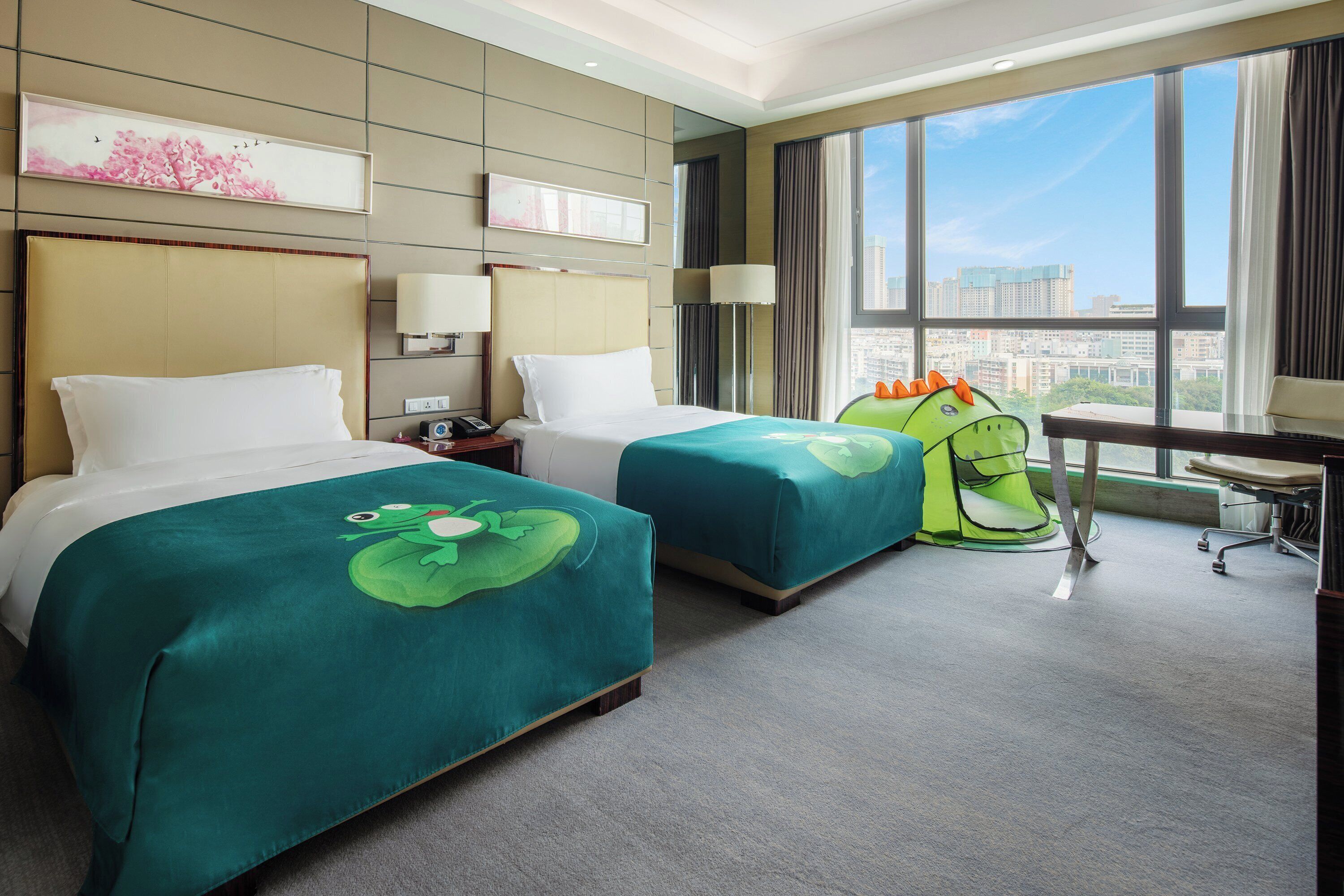 A hotel room with two beds, a desk, and a view of the city.