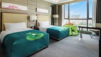 A hotel room with two beds, a desk, and a view of the city.