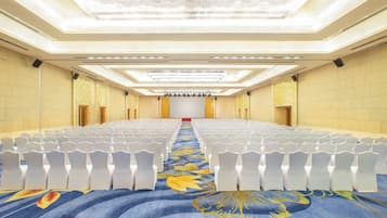 Une salle de conférence avec des rangées de chaises blanches, une moquette à motifs floraux et un grand écran à l’avant.
