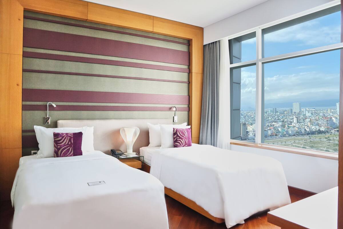 A hotel room with two beds, a city view, and a modern design.