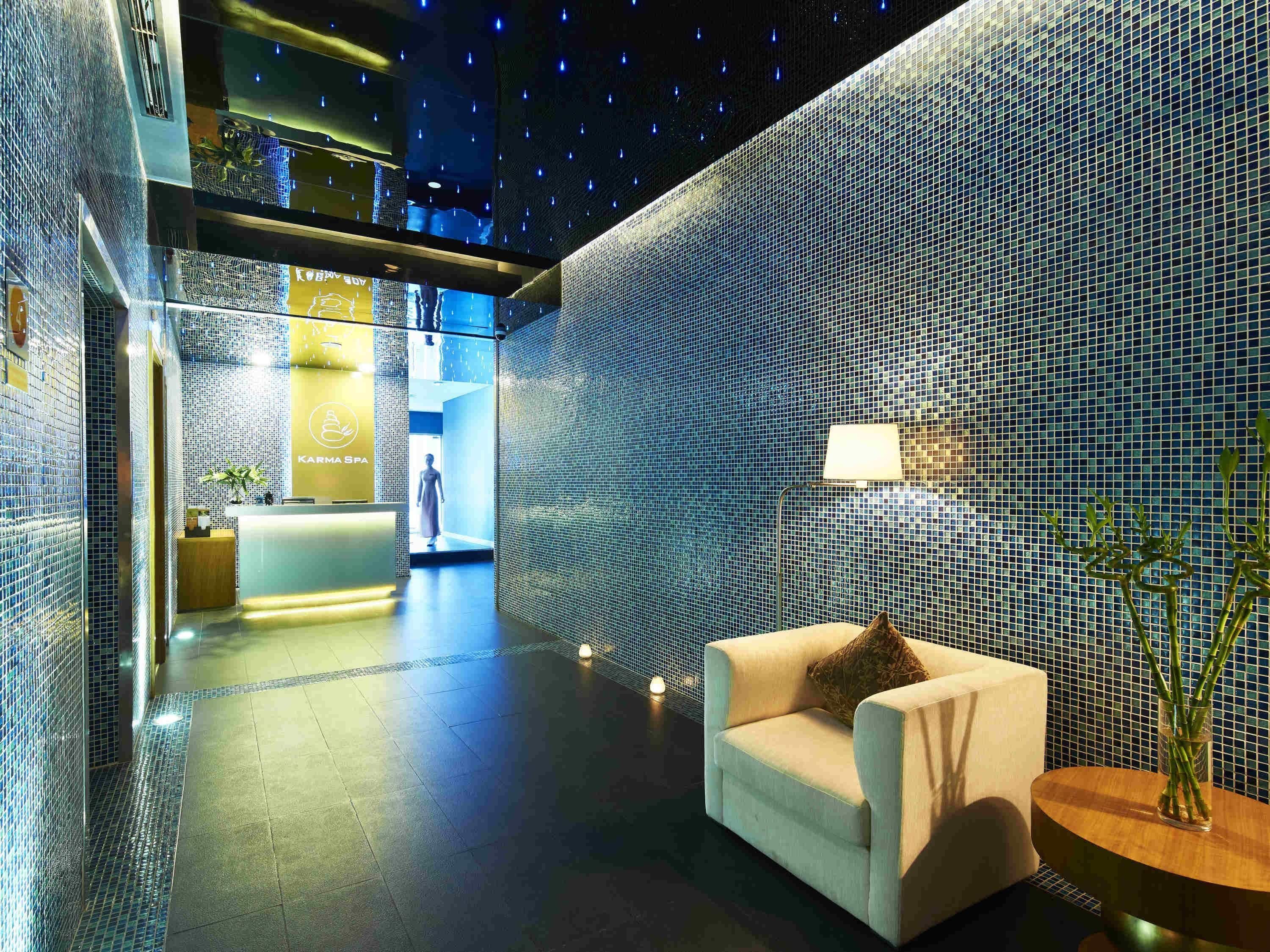 A modern spa interior with a reception desk, a seating area with a lamp, and a mosaic wall.