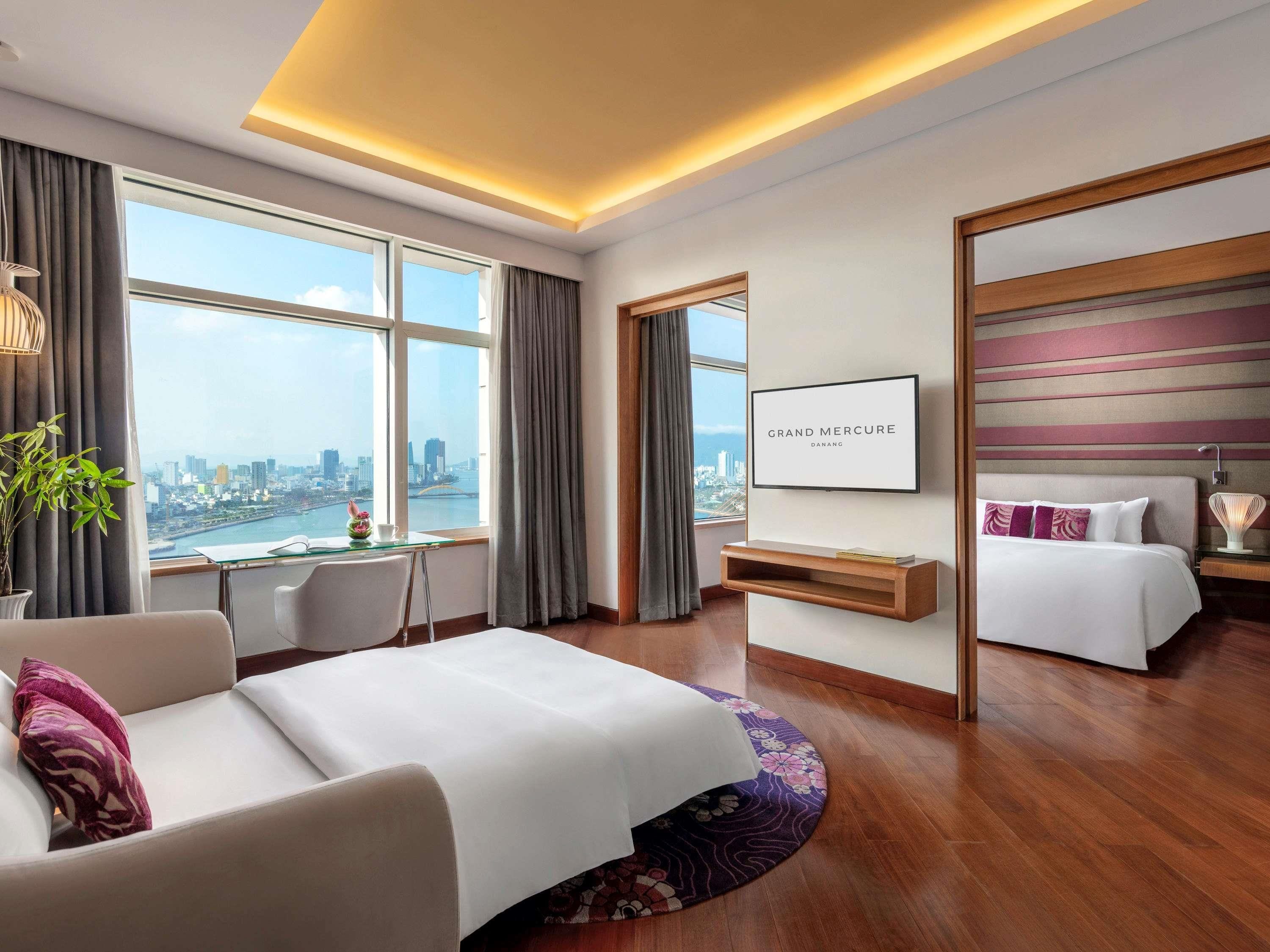A hotel room with a bed, a desk, a chair, a TV, and a view of the city.