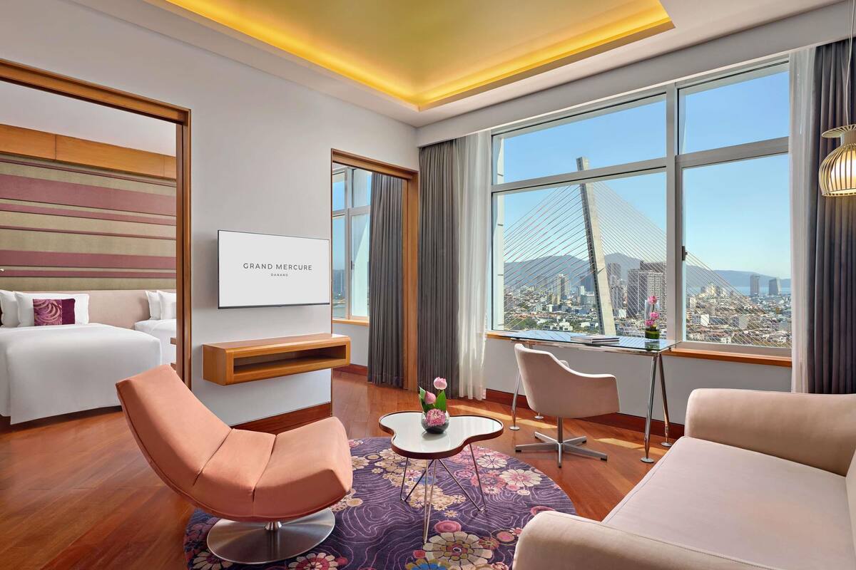A modern hotel room with a large window, a bed, a desk, and a chair.