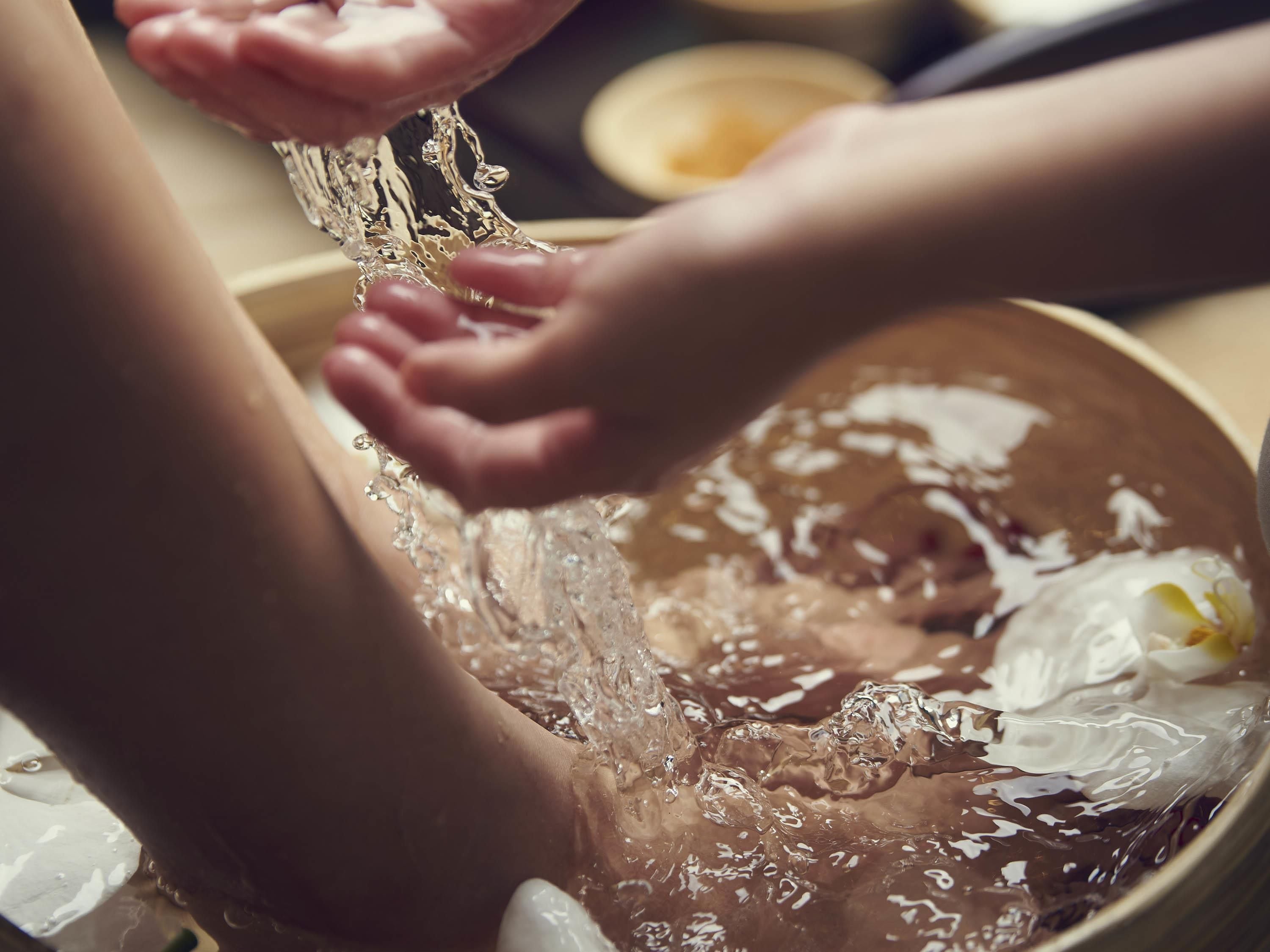 A close-up of hands washing in a bowl with water and soap.