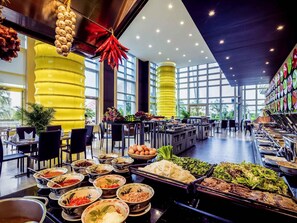 A buffet with various food items, a yellow pillar, and a large window. - Grand Mercure Danang (Da Nang)