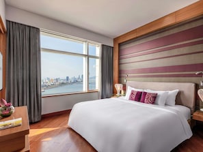 A hotel room with a large bed, a view of a cityscape, a wooden floor, and a modern headboard. - Grand Mercure Danang (Da Nang)