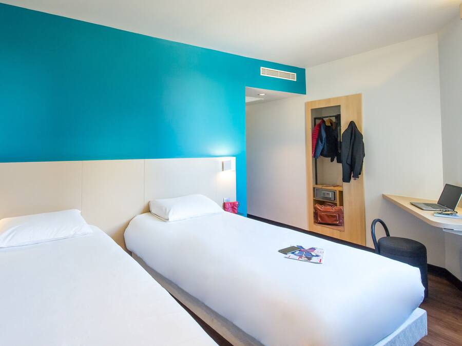 Habitación de hotel con dos camas, un escritorio con una computadora portátil y un perchero con ropa.