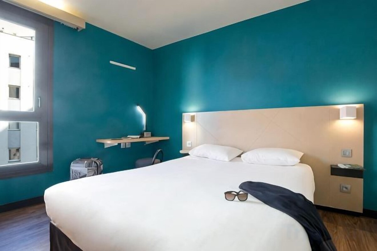 Une chambre d’hôtel avec un grand lit, une table de chevet, un bureau, une chaise et une fenêtre.