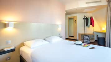 A hotel room with a bed, bedside tables, a mirror, a coat rack, and a desk with a lamp.