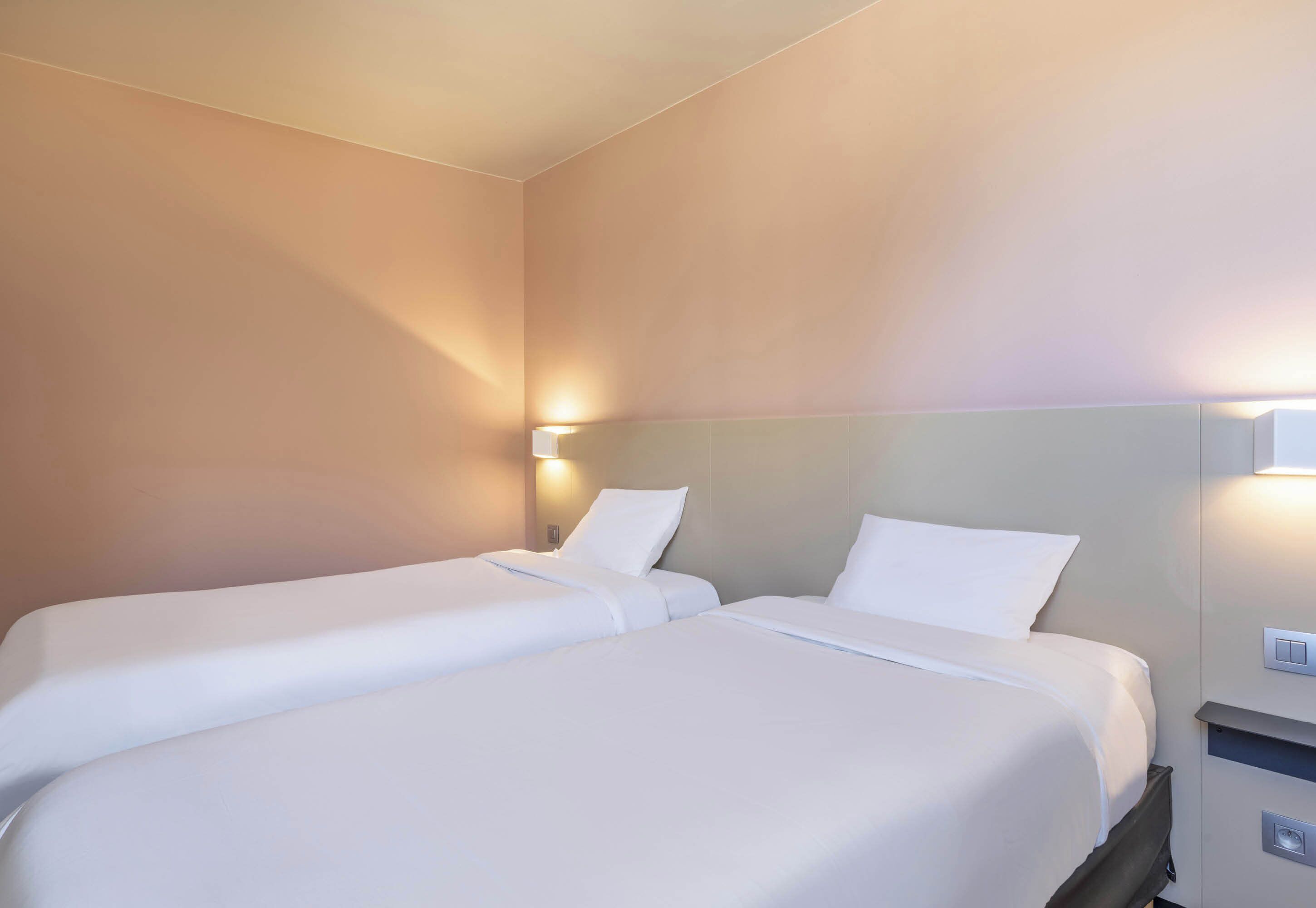 Habitación de hotel con dos camas individuales, una mesita de noche y una lámpara fijada en la pared.