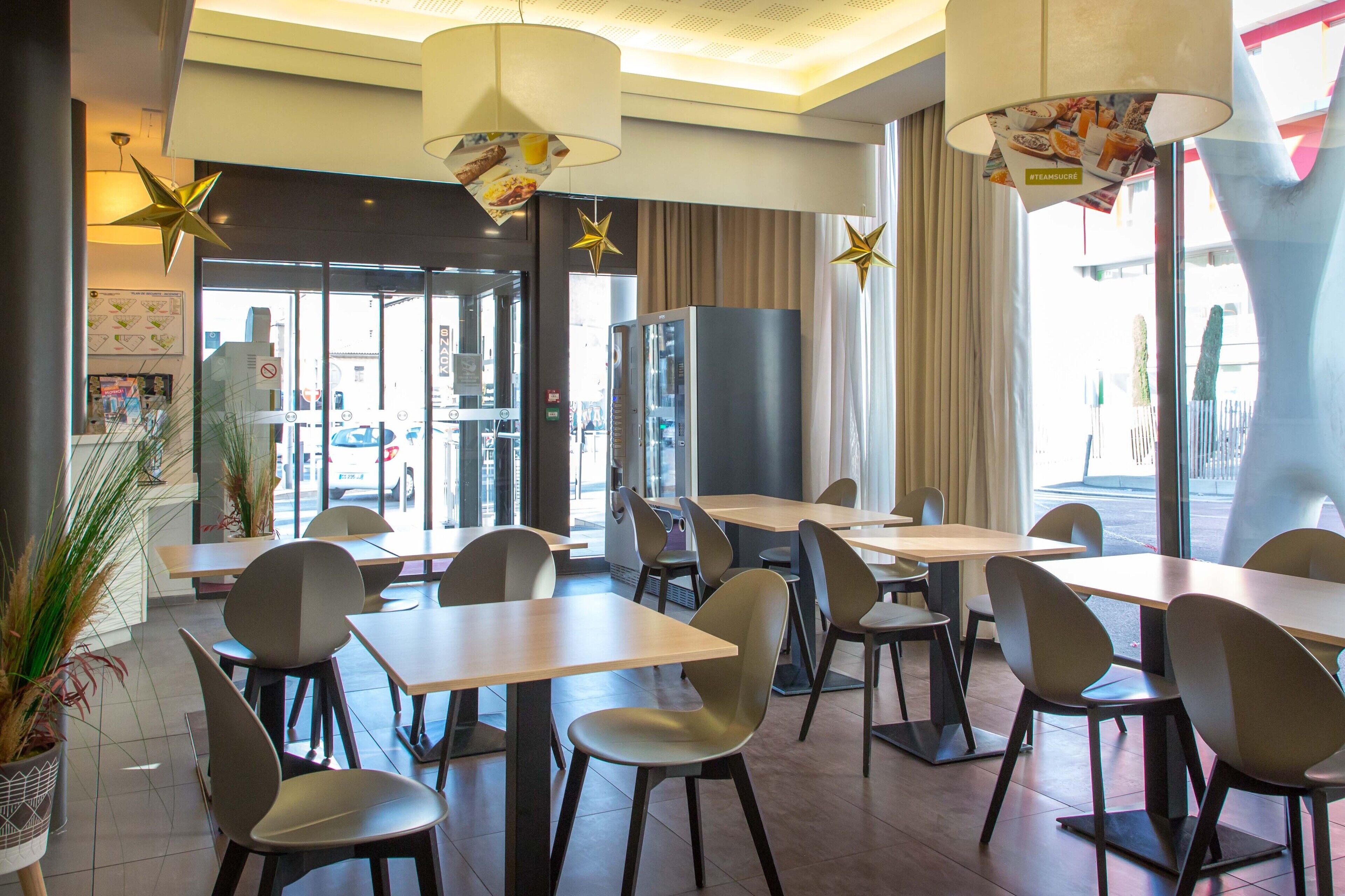 A modern restaurant interior with tables and chairs, large windows, and decorative star-shaped lights.