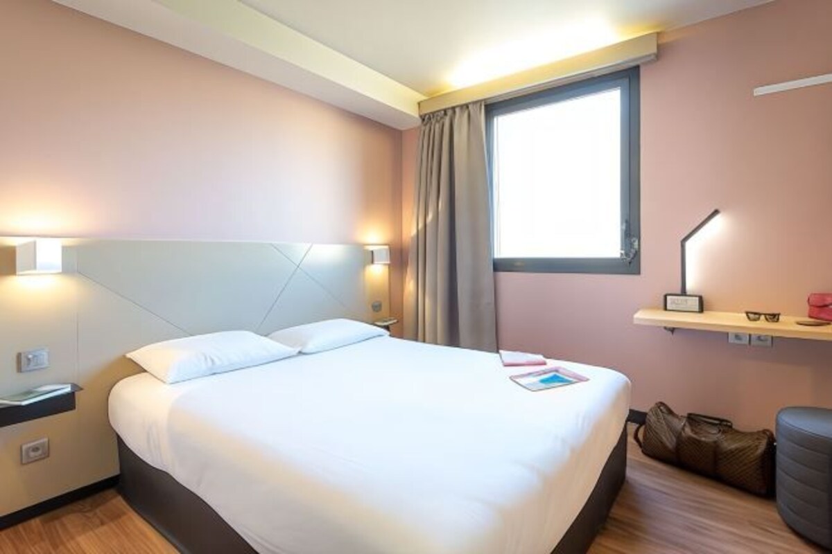 Una habitación de hotel con cama, lámparas de noche, una ventana, escritorio y una silla.