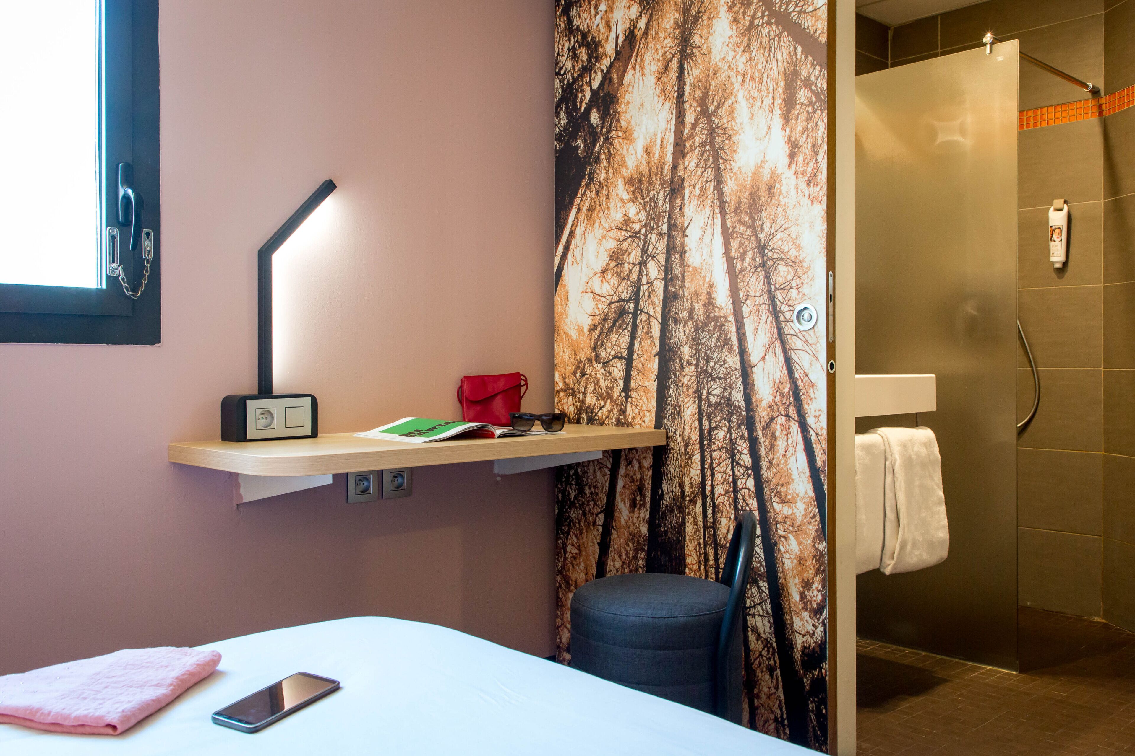 Ein Hotelzimmer mit Bett, Nachttisch mit Lampe, Stuhl, Duschbereich und Handtuchhalter.
