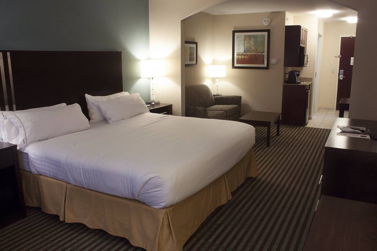 Ein Hotelzimmer mit einem großen Bett, Nachttischen, einem Schreibtisch, einem Stuhl und einer kleinen Küchenzeile.