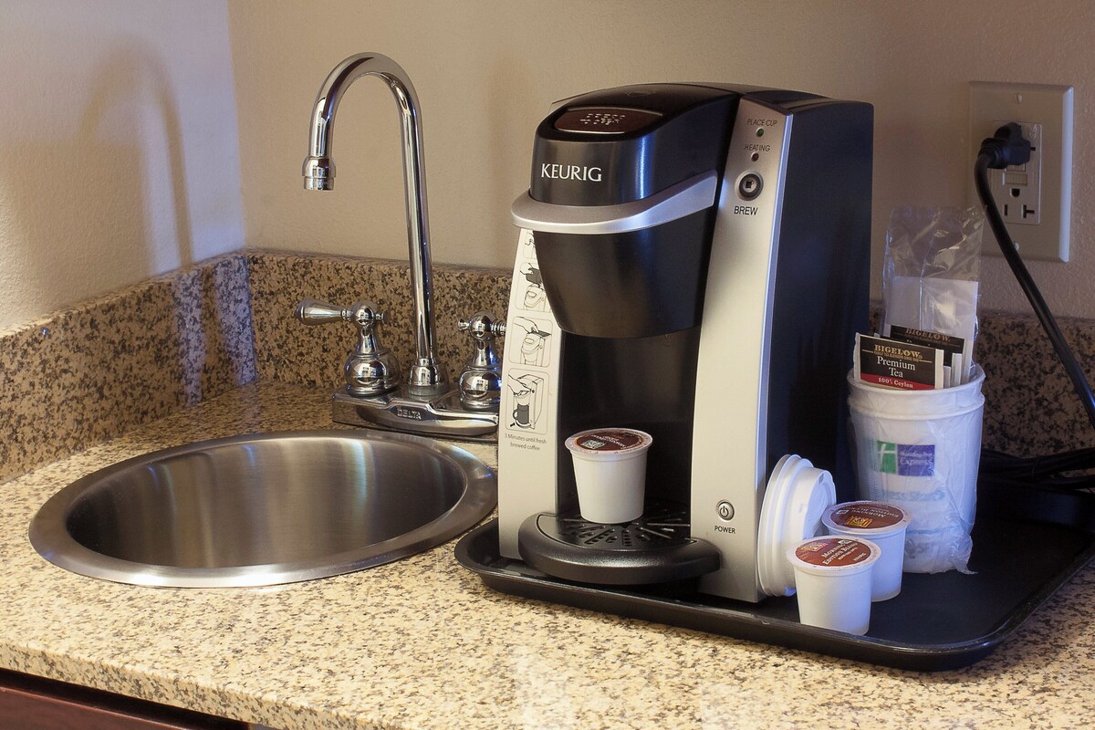 Keurig-kahvinkeitin, jossa on tippalauta, pesuallas ja paketti Bigelow-premiumteetä.