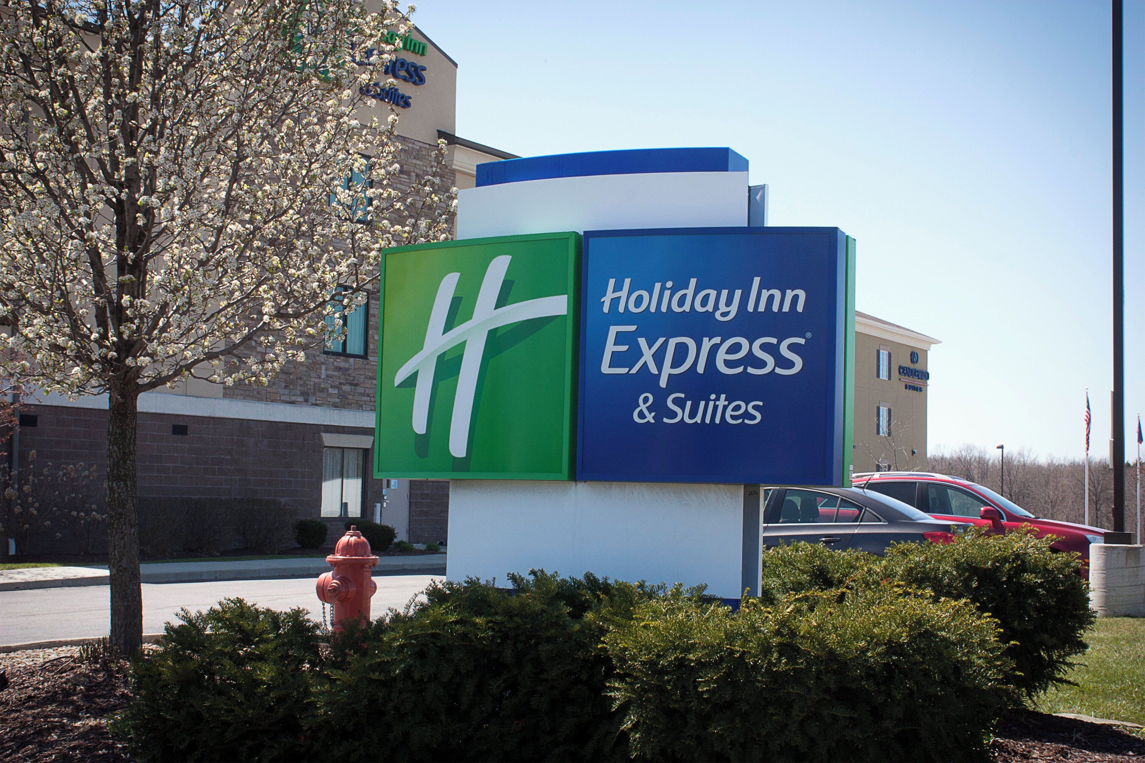 Señal de Holiday Inn Express & Suites con una vista clara de la entrada del edificio y un hidrante rojo al frente.