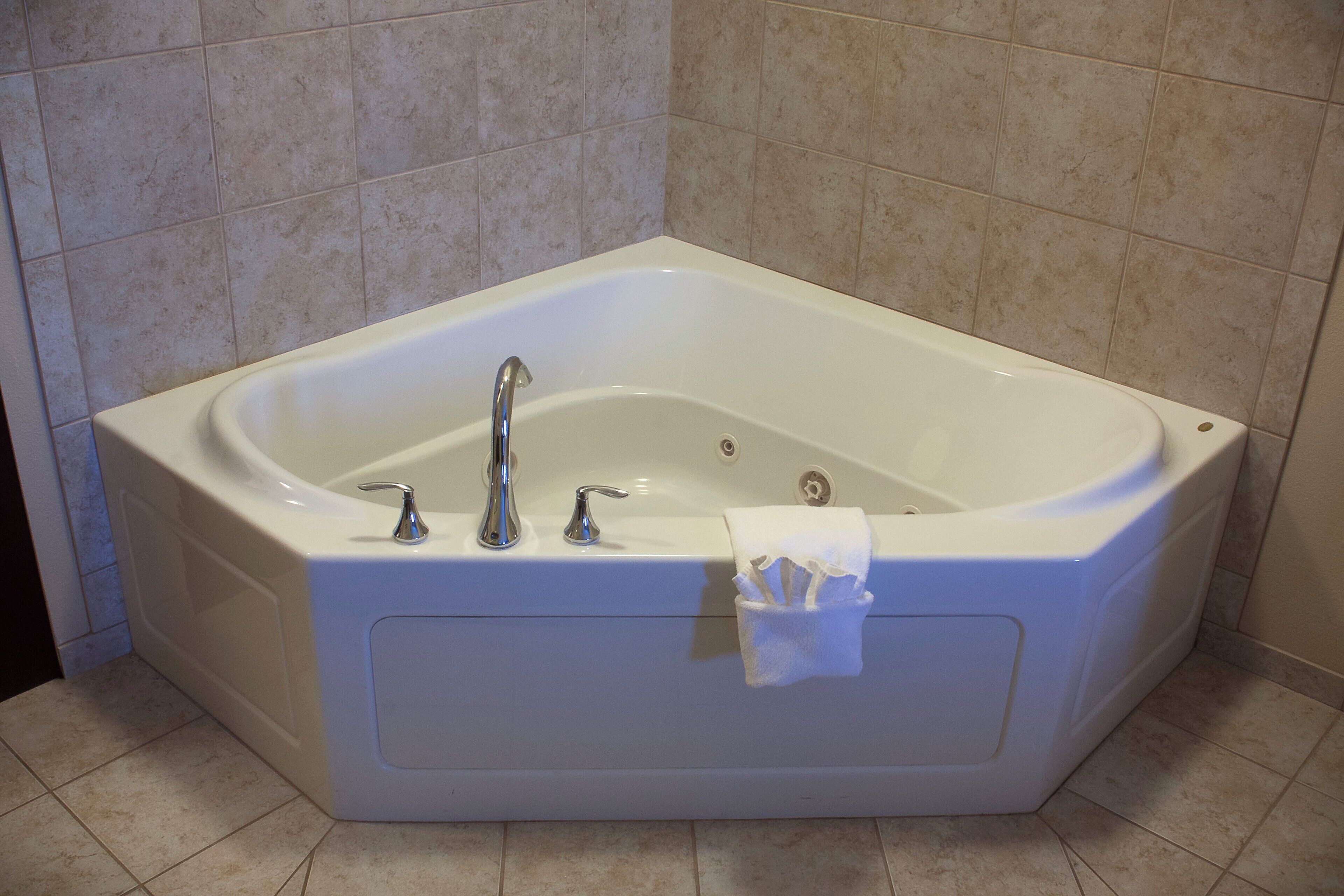 Una vasca da bagno ad angolo con due rubinetti, uno scarico e un porta asciugamani.