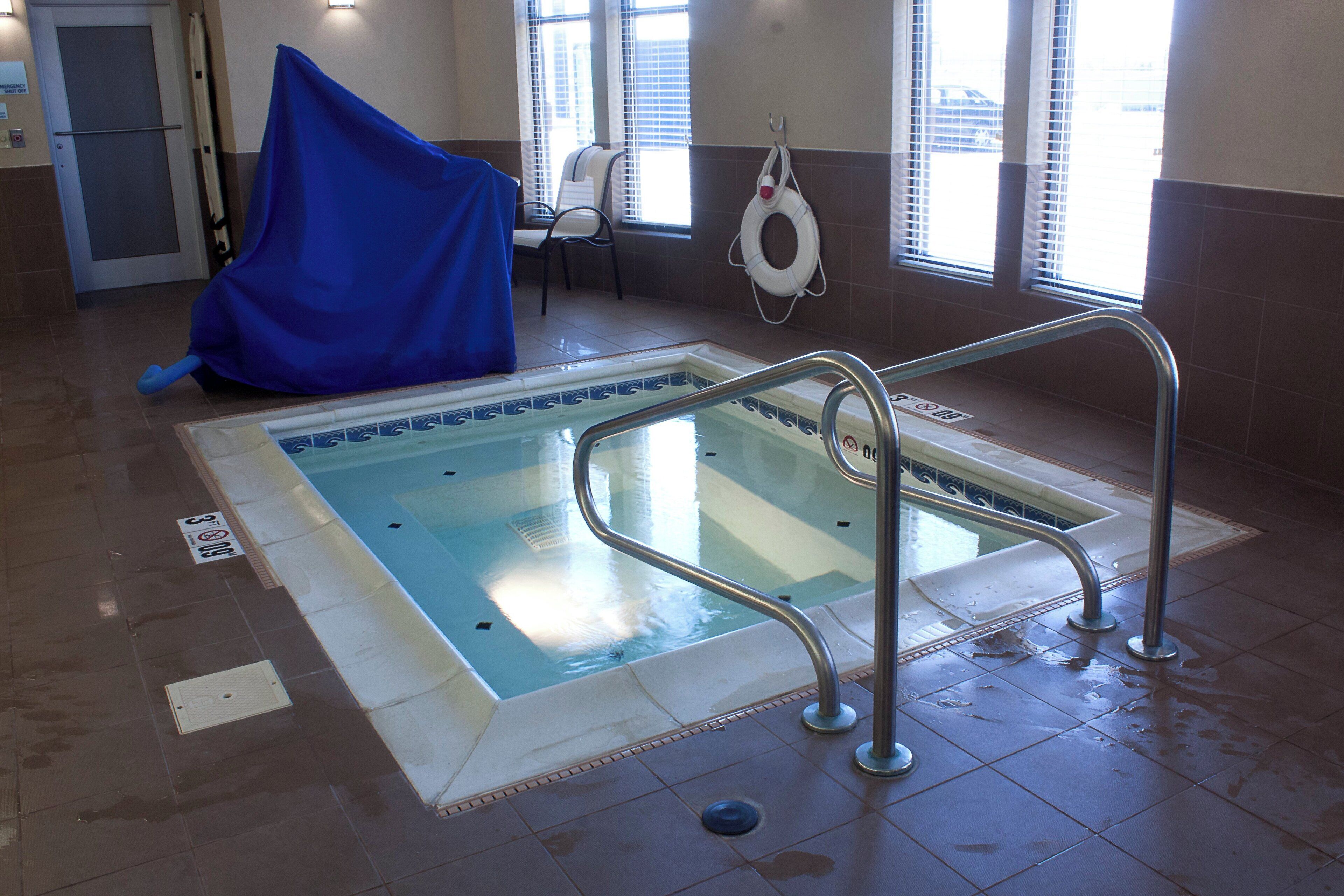 Uma piscina interior com chão em mosaico, um flutuador preso na parede e uma cobertura azul sobre a piscina.