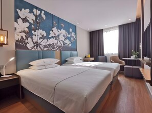 A hotel room with two beds, a large floral painting, a desk, a chair, and a window with curtains.