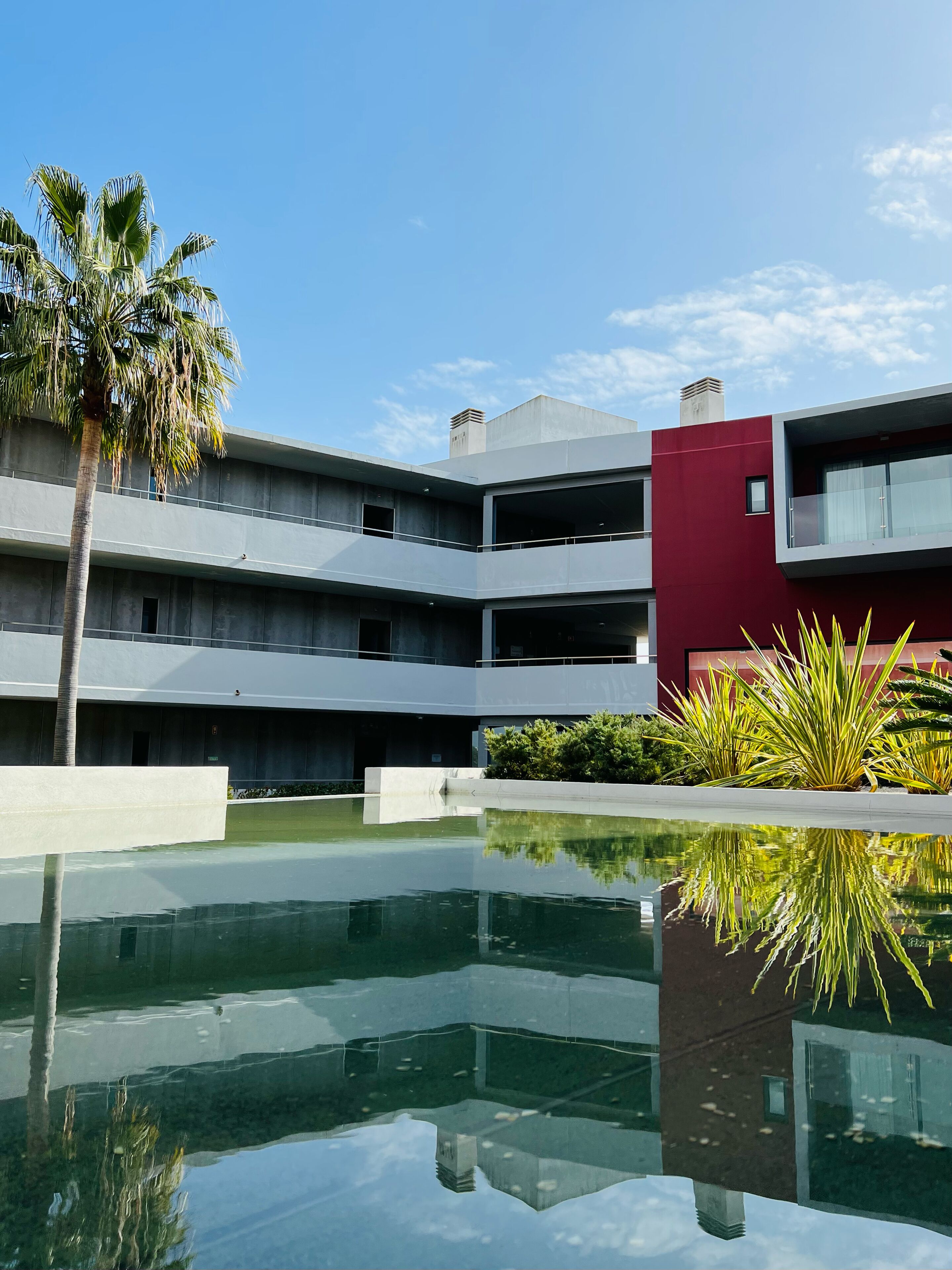 A modern building with multiple balconies and a reflective pool.