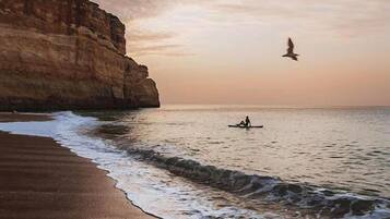 A beach with a cliff, waves, and a person in a kayak.
