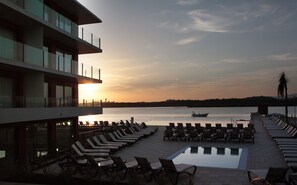 A poolside area with lounge chairs and a view of the sunset over a body of water.