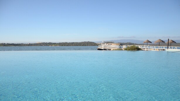 Une magnifique piscine à débordement d’un bleu profond, offrant une vue sur une côte lointaine et un bateau.