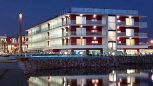 Un hôtel à plusieurs étages doté de balcons, d’un espace piscine et dont l’image se reflète dans l’eau.