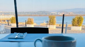 Une table avec une tasse et de la nourriture, donnant sur une étendue d’eau et des collines lointaines.