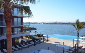 A modern hotel with a pool, sun loungers, and a view of the sea.