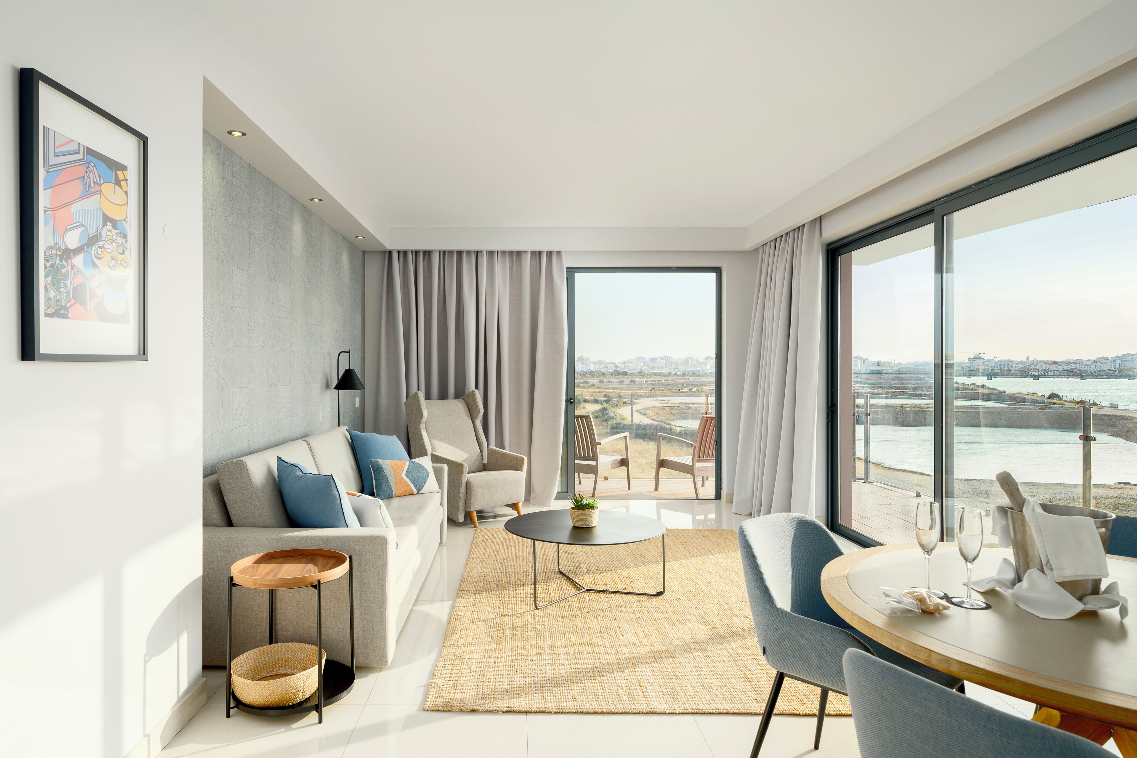 A modern living room with a sofa, armchairs, a coffee table, and a view of the sea.