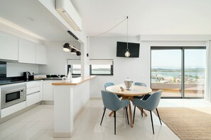 A modern kitchen with a dining area, a large window with a view, and a flat-screen TV mounted on the wall.